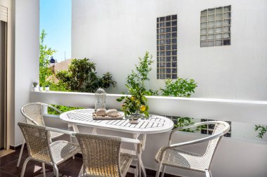 Mobilyalı balkon, fenerle süslenmiş beyaz masa, mumlar ve limon dalı, dört sandalye, güneşli yaz günü, tatil konsepti..