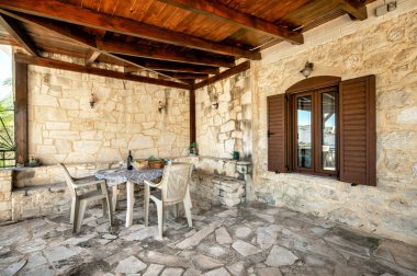 Taştan Kır Evi 'nin arka bahçesi: Kırsal bir taşra evinin arka bahçe terası huzurlu bir manzarası. Alan basit bir açık hava masası ve sandalyelerle süslenmiş, rahatlama ve açık hava toplantıları için sakin bir ortam yaratıyor.