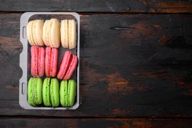 Ev yapımı renkli badem kurabiyesi seti, plastik pakette, eski koyu ahşap masa zemininde, en üstteki düz görünümde, metin alanı için kopyalama alanı ile birlikte.