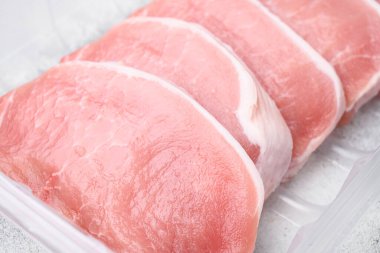 Pişmemiş domuz pirzolası seti, plastik paket konteynırında, gri taş masa arkasında.