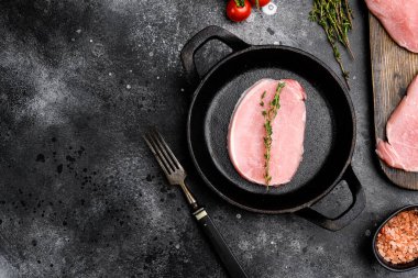 Pişmemiş domuz pirzolası seti, kızgın demir tavada, siyah taş masa zemininde, üst görünüm düz, metin alanı için fotokopi alanı