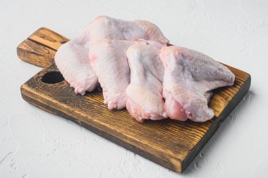 Pişmemiş tavuk kanatları seti, ahşap kesim tahtası, beyaz taş arka plan