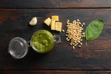 İçinde parmesanlı fesleğen ve çam fıstığı bulunan cam kavanozda ev yapımı pesto. Koyu ahşap masa tahtalarının üzerinde..