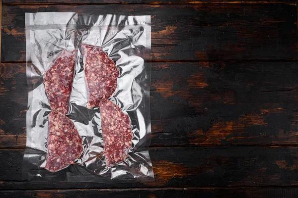 Beef patties in a vacuum packing, on old dark  wooden table background, top view flat lay, with copy space for text