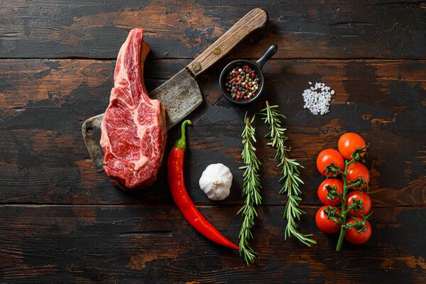 Raw Delmonico steak on meat cleaver. Organic farm marbled prime black angus beef. Dark wooden background. Top view. With seasonings, peppercorns, chilie, rosemary,salt,garlic.  Noone