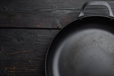 Metin ya da yiyecek için kopyalama alanı ya da yiyecek alanı olan boş demir tava seti, üst görünüm düz, siyah ahşap masa arkaplanı üzerinde