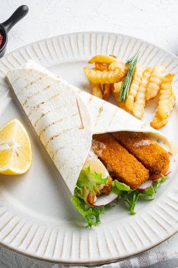 Balık kroket, peynir ve sebzeli tortilla rulosu. Tabakta, beyaz arka planda.