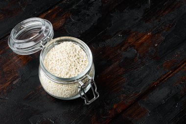 Cam kavanozda dekore edilmiş susam tohumları, eski koyu ahşap masa arka planında, metin alanı ve yeri ile