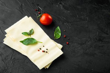 Lazanya hamuru seti, baharat ve otla, siyah taş zemin üzerinde, metin için kopya alanı ile