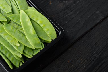 Şekerli bezelyeler, taze olgun bebek kabukları, plastik kabın içinde, siyah ahşap arka planda, kopyalanacak yer ve metin için yer var.