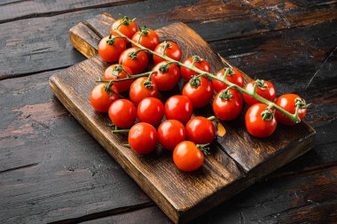 Tahta kesme tahtasının üzerinde, eski, koyu ahşap masa zemininde taze kırmızı domates kümesi.
