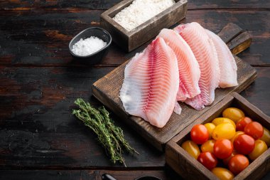 Çiğ beyaz tilapia balığı, basmati pilavı ve kiraz domatesli malzeme, koyu ahşap zemin üzerinde metin alanı için fotokopi alanı