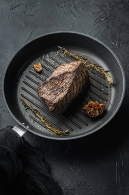 Kızarmış demir tavada, siyah arka planda mermer biftek pişirme seti.