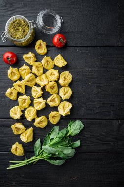 Fesleğen ve çam ezmeli çiğ Tortellini, siyah ahşap masa arkaplanı, üst görünüm düz, metin için kopyalama alanı ile