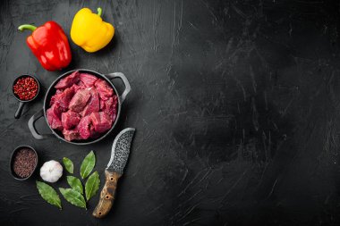 Biftek yahnisi hammaddesi, tatlı dolma biberli, dökme demir kızartma tavasında, siyah taş zemin üzerinde, üst görünüm düz, metin için kopyalama alanı ile birlikte.