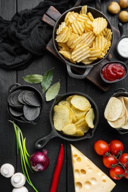 Peynir ve soğanlı farklı patates cipsi çeşitleri, siyah ahşap arka planda, üst manzara düz.