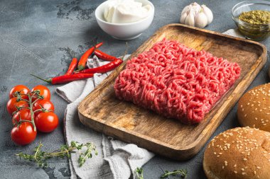 Baharatlı taze kıymalı biftek burgerleri, ahşap tepside, gri taşlı arka planda.