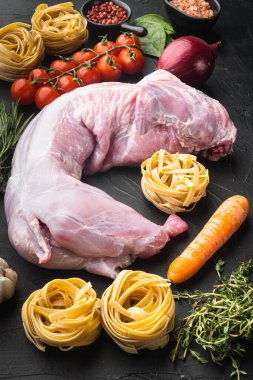 Çiğ tavşan eti ve taze sebzeler, pişmeye hazır, siyah taş arka planda.