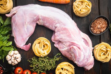 Çiğ tavşan eti ve taze sebzeler yemek için hazır, eski siyah ahşap masa arka planında, üst manzara düz yatıyordu