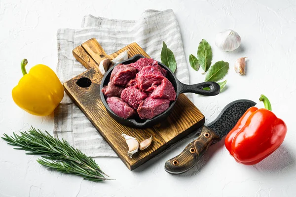 Fresh raw beef cubes set with sweet bell pepper, in cast iron frying pan, on white stone  surface