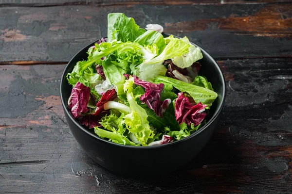 Farklı marul salatalarından taze yapraklar, eski siyah ahşap masa arka planında.