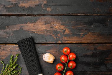 Pişmemiş siyah spagetti ve malzeme seti, eski koyu ahşap masa arkaplanı, üst görünüm düz, metin alanı için kopyalama alanı ile