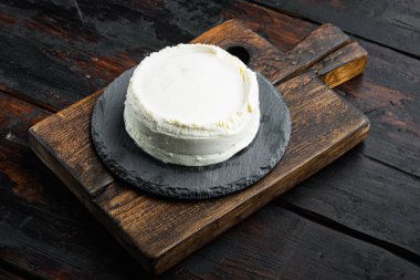 Taze, ricotta peyniri, ahşap kesim tahtasının üzerinde, eski, siyah masa arkasında.