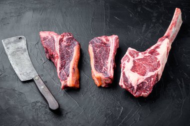 Kurumuş çiğ et seti, tomahawk, biftek ya da biftek, eski kasap bıçağı, siyah taş arka planda.