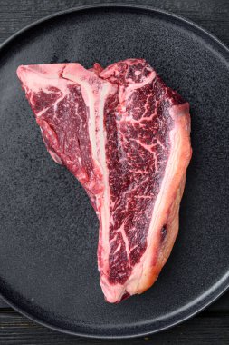 Izgara ya da barbekü için T-bone ya da Biftek seti, tabakta, siyah ahşap masa zemininde, üst görünüm düz yatıyordu