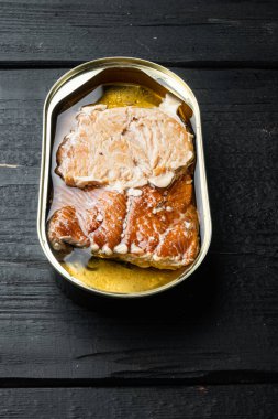 Konserve füme alabalık filetosu seti, teneke kutuda, siyah ahşap masa arkasında.