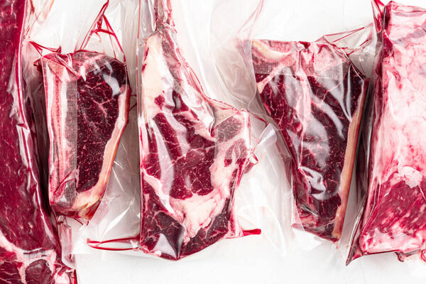 Raw marbled beef steak in vacuum packaging set, tomahawk, t bone, club steak, rib eye and tenderloin cuts, on white stone  background, top view flat lay