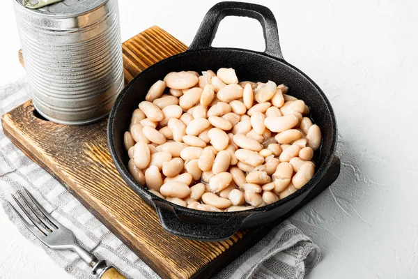 White canned beans set, with metal can, in cast iron frying pan, on white stone  surface