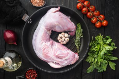 Zeytinyağlı, biberiyeli, biberiyeli taze çiğ tavşan, dökme demir tavada, siyah ahşap masa zemininde, düz manzaralı