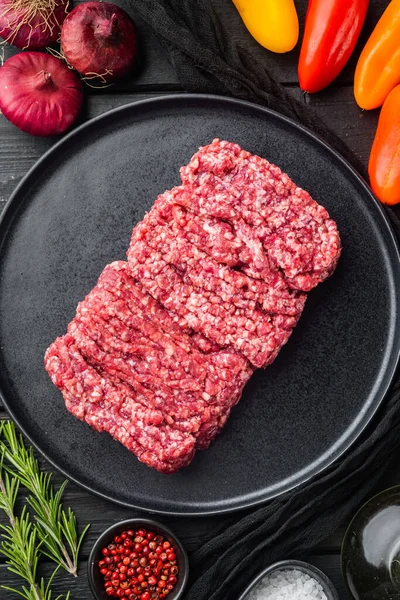 Taze, kıymalı biftek, siyah ahşap masa arkasında, üst manzara düz.