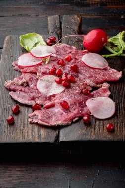 Klasik sığır eti carpaccio seti, turp ve garnet, ahşap servis tahtasının üzerinde, eski siyah ahşap masa arkasında