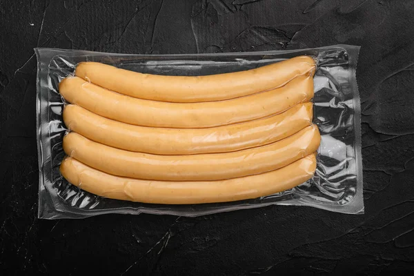 Raw chicken sausages in vacuum package set, on black dark stone table background, top view flat lay