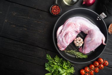 Zeytinyağlı taze çiğ tavşan, biberiye, biber, deniz tuzu, soğan seti, dökme demir kızartma tavasında, siyah ahşap masa zemininde, üst görünüm düz, metin için fotokopi alanı