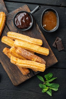 Geleneksel churros çubukları tarçın ve şeker tozu seti, siyah ahşap masa arkaplanı, üst görünüm düz