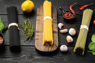 Siyah ahşap masa zemininde, renkli, çiğ spagetti seti.