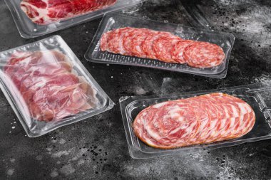 Süpürge paketlenmiş sucuklu Prosciutto salam seti, arka planda siyah taştan masa.