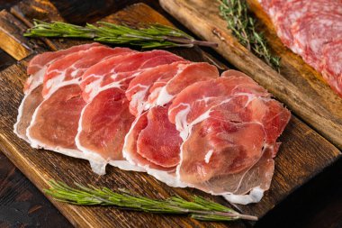 Yıllanmış et jamonu, kurumuş sosis dilimleri, eski, siyah ahşap masa arka planında.