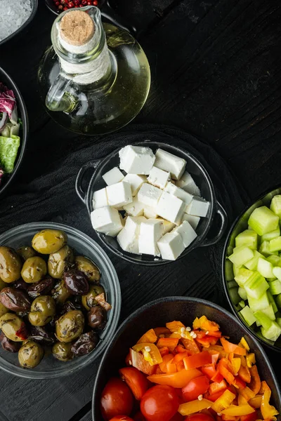 Geleneksel Yunan salatası, domates, soğan, zeytin, feta peyniri için malzemeler, siyah ahşap masa zemininde, üst görünüm düz.