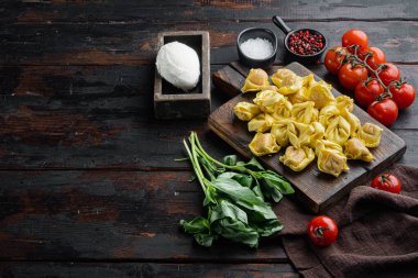 Peynir ve fesleğen setiyle ev yapımı Tortellini, ahşap kesme tahtasında, eski siyah ahşap masa zemininde, metin için fotokopi alanı ile