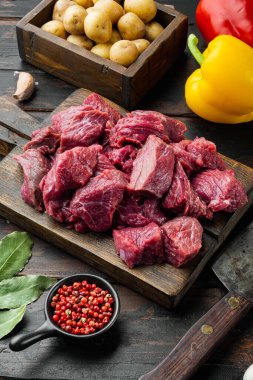Gulaş için ham malzemeler. Koyu ahşap masada tatlı dolmalık biber ve patatesli taze kesilmiş et.