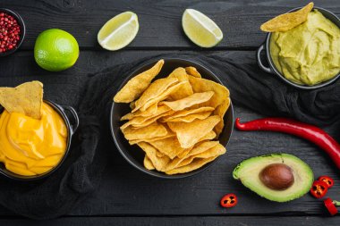 Nachos and guacamole and cheese sauces, on black wooden background, top view or flat lay
