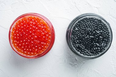Glass jar with black and red caviar, on white background, top view flat lay