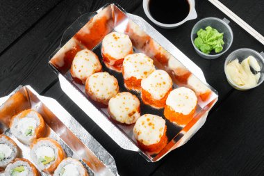 Take away sushi rolls in containers, philadelphia rolls and baked prawn rolls set, on black wooden table background