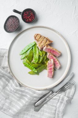 Grilled Ahi Tuna Steak set with spring onions and sugar snap peas, on plate, on white stone  background, top view flat lay