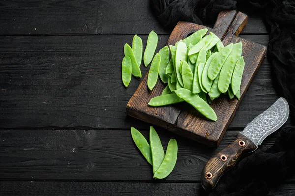 Organic Green Sugar Snap Peas Ready to Eat set, on wooden cutting board, on black wooden background , with copyspace  and space for text