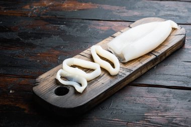 Raw squid, sliced for rings on cutting board over dark rustic wooden background, food photo.